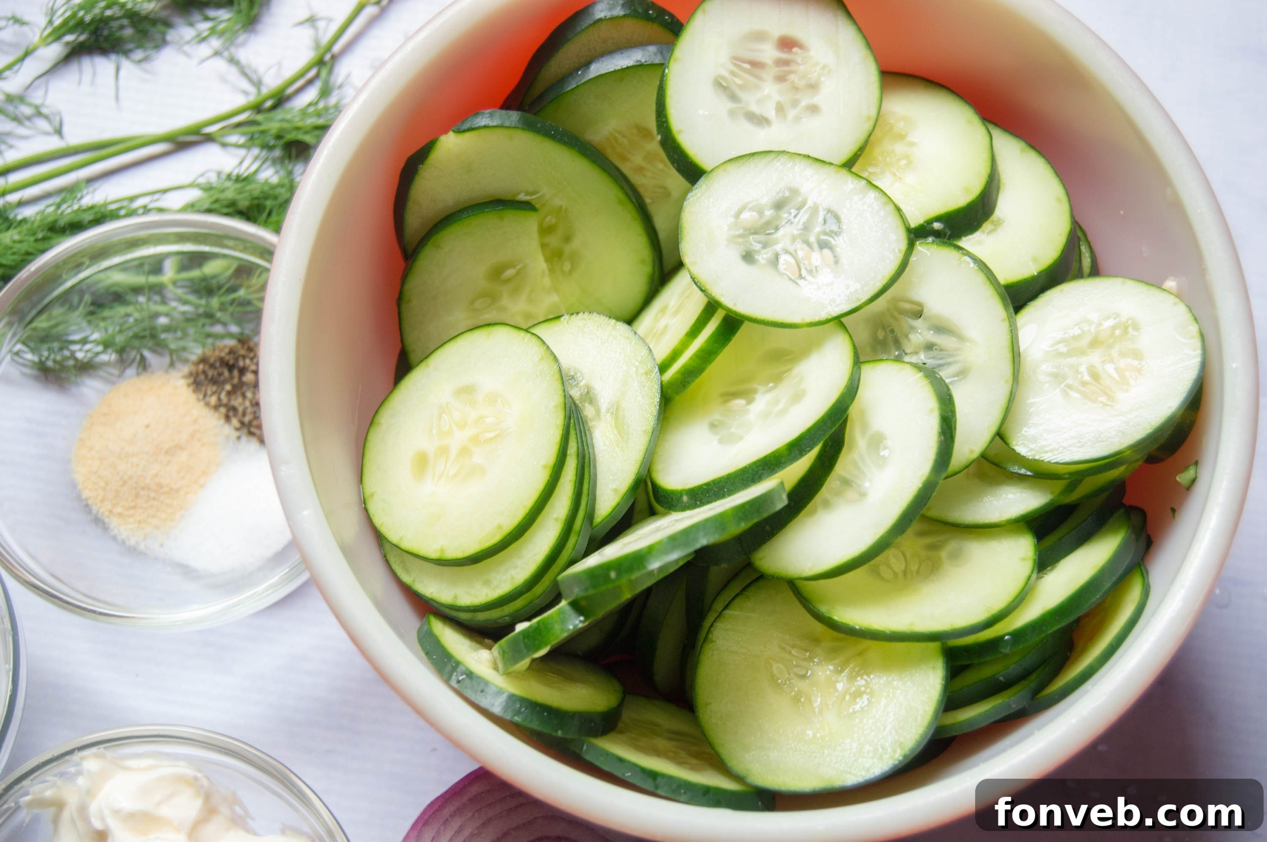 Close-up of thinly sliced cucumbers and red onion, tossed in a creamy dressing, capturing the texture and freshness of the salad.