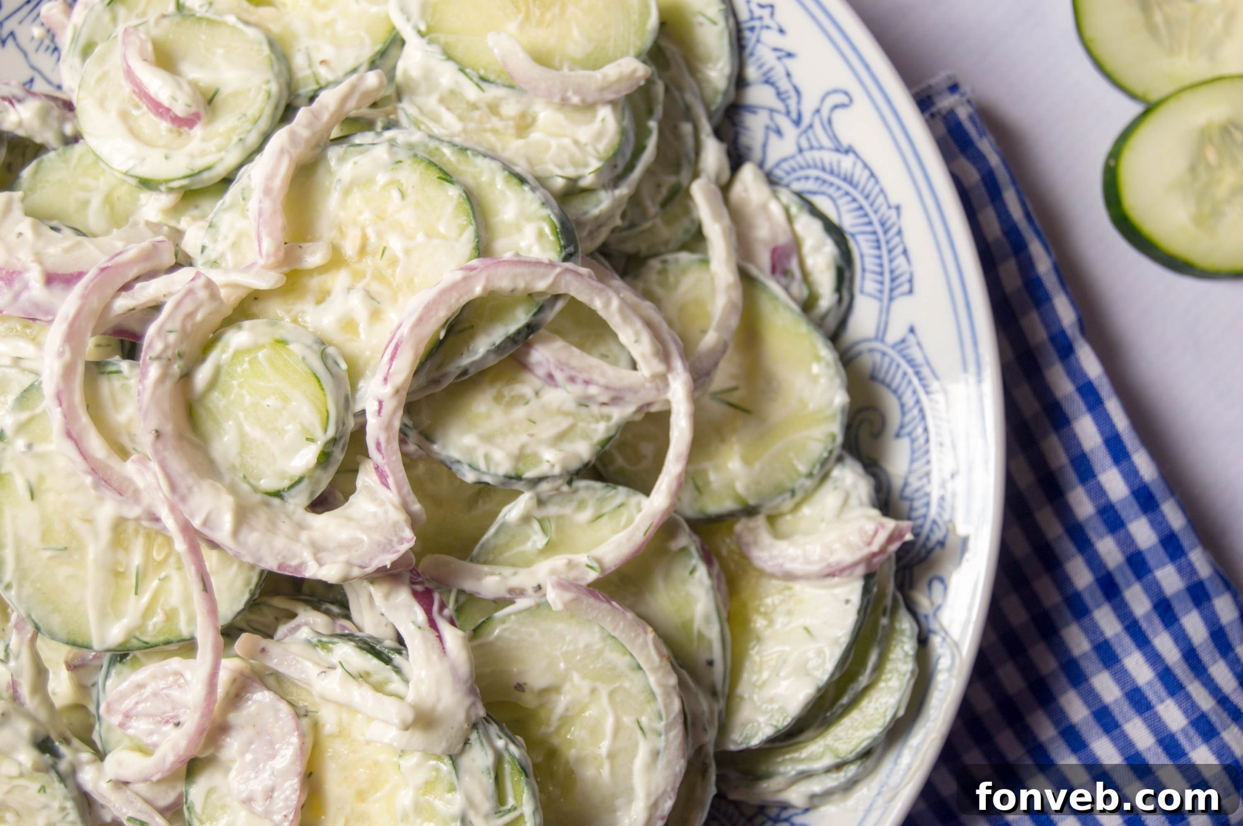A bowl of creamy cucumber salad on a rustic outdoor table setting, suggesting a perfect summer meal.