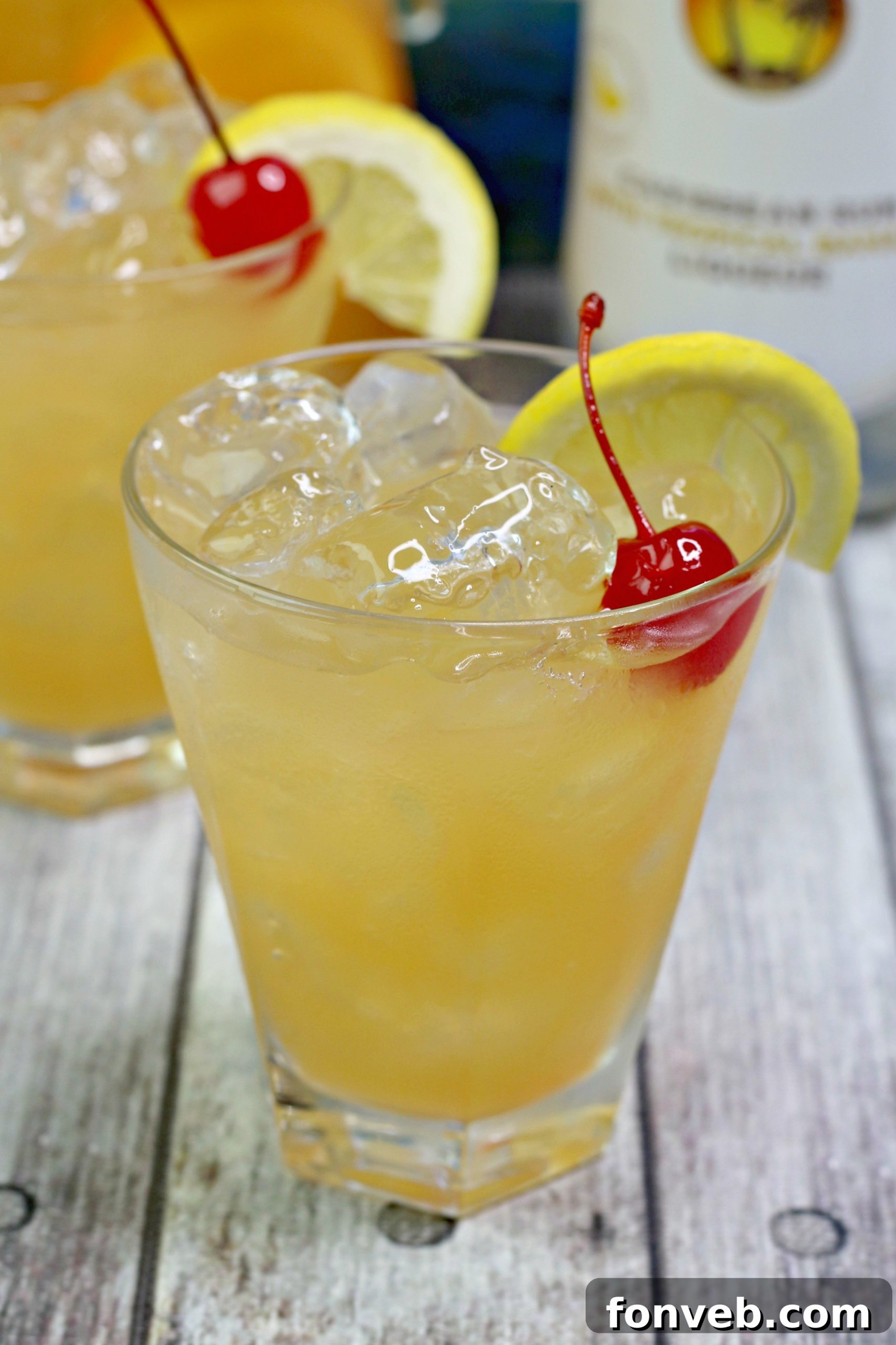 A hand holding a glass of banana rum punch, showing its vibrant color