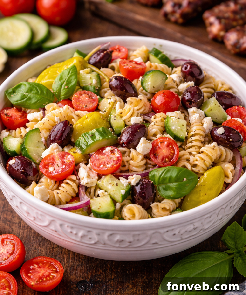 A beautifully presented Greek Pasta Salad in an elegant white bowl, showcasing vibrant colors of fresh vegetables, pasta, and feta cheese.