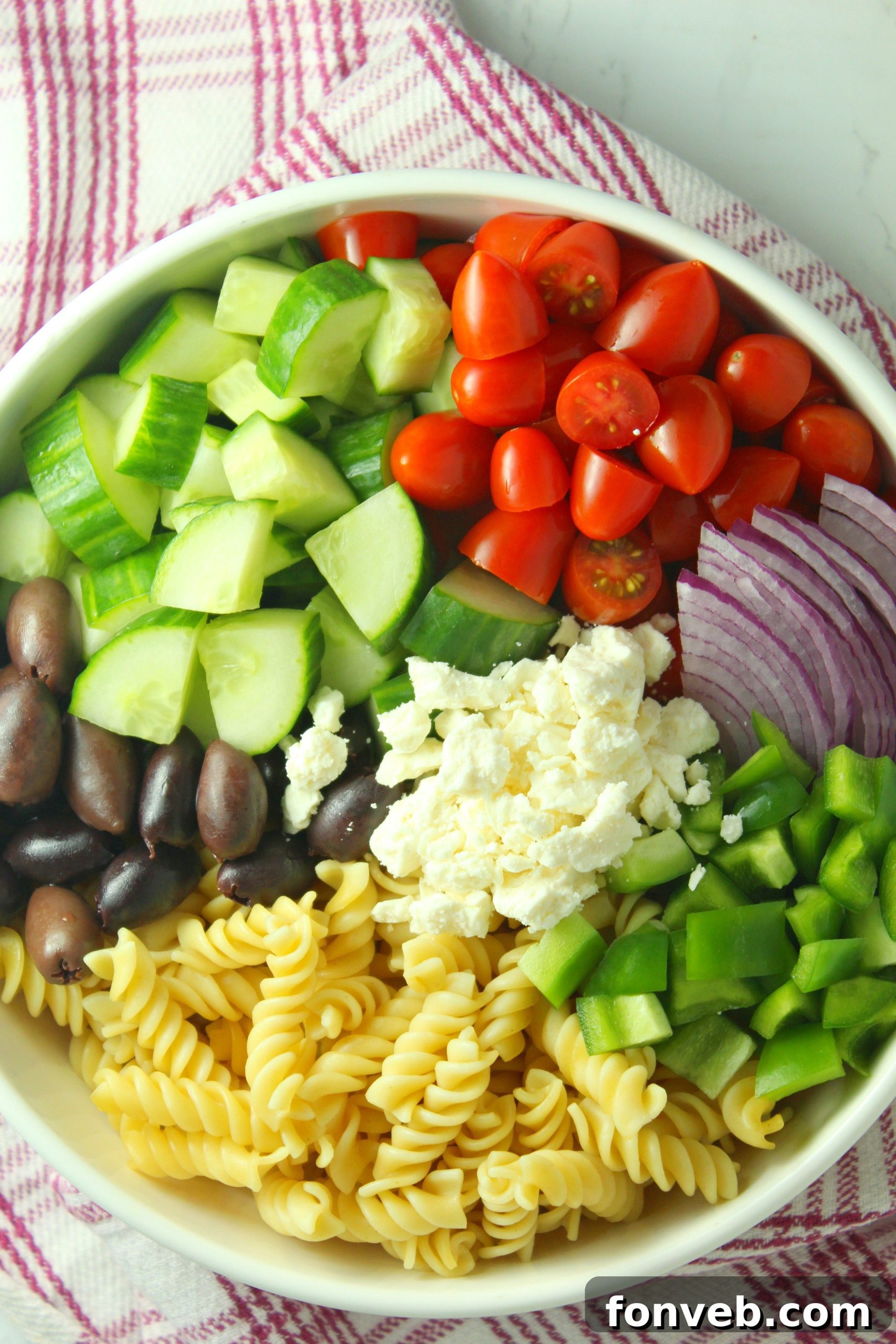 A serving spoon lifting a portion of Greek Pasta Salad, showcasing the pasta and vegetables.