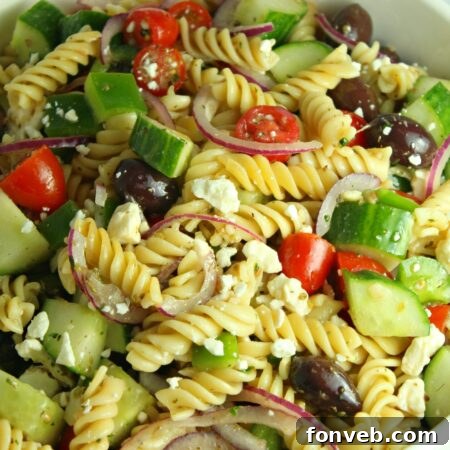 A close-up of a serving of Greek Pasta Salad with a spoon, highlighting its inviting texture.