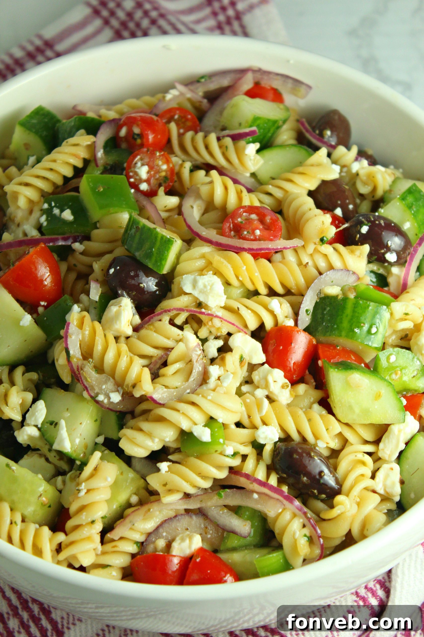 Close-up of Greek Pasta Salad in a pretty white bowl, highlighting the fresh cucumbers, feta, and tomatoes.