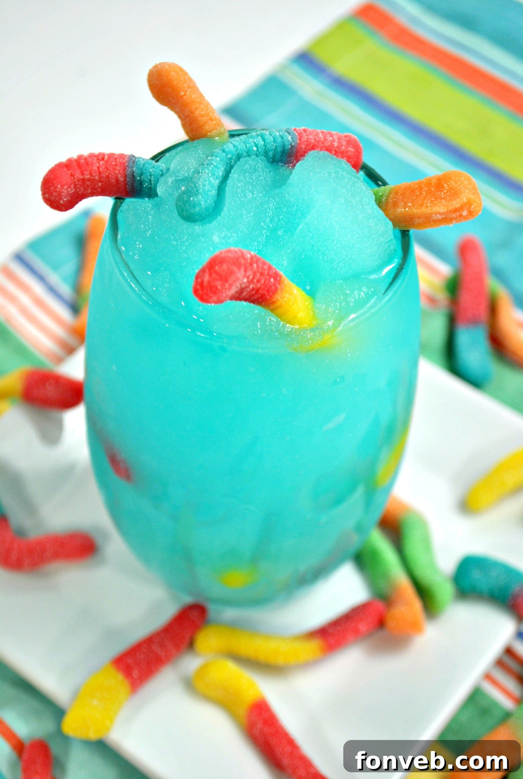 A vibrant blue Drunken Sour Gummy Worm Cocktail with many colorful gummy worms spilling out of the glass, ready to be enjoyed.