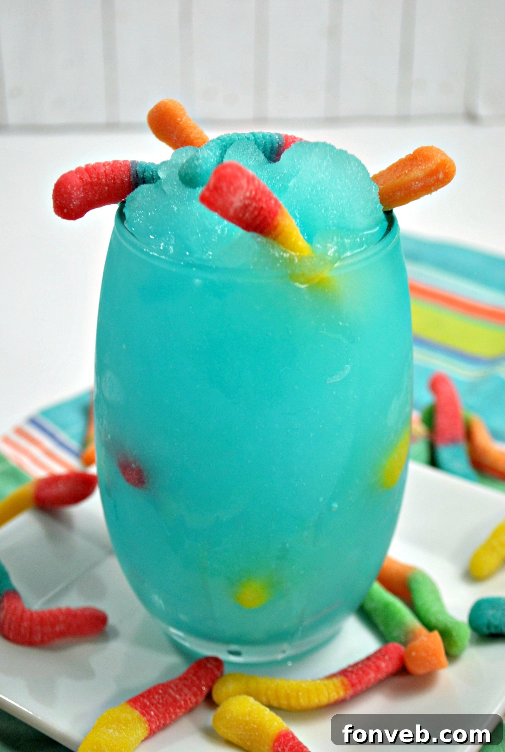 A whimsical arrangement of the Drunken Sour Gummy Worm Cocktail, featuring the drink next to a scattering of sour gummy worms, emphasizing its playful nature.