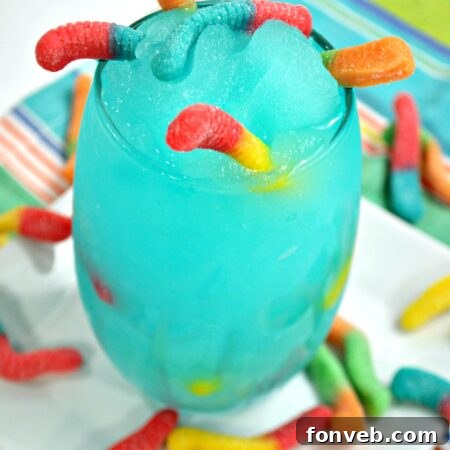A close-up of the completed Drunken Sour Gummy Worm Cocktail with a vibrant blue color and many sour gummy worms.