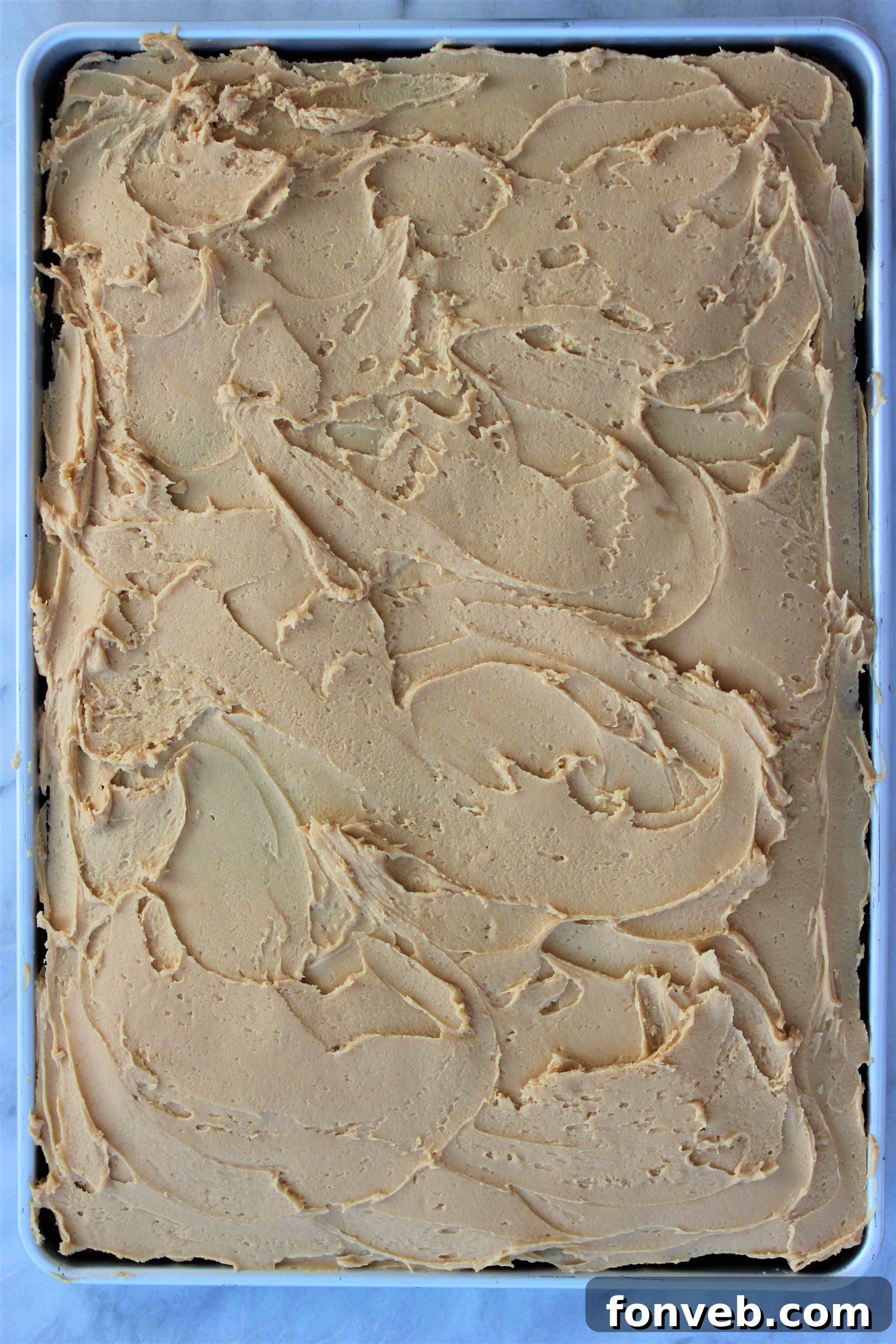 Ultimate Peanut Butter Texas Sheet Cake 4 A large rectangular Texas Sheet Cake sitting on a cooling rack, freshly frosted with a thick layer of peanut butter frosting, ready for serving.