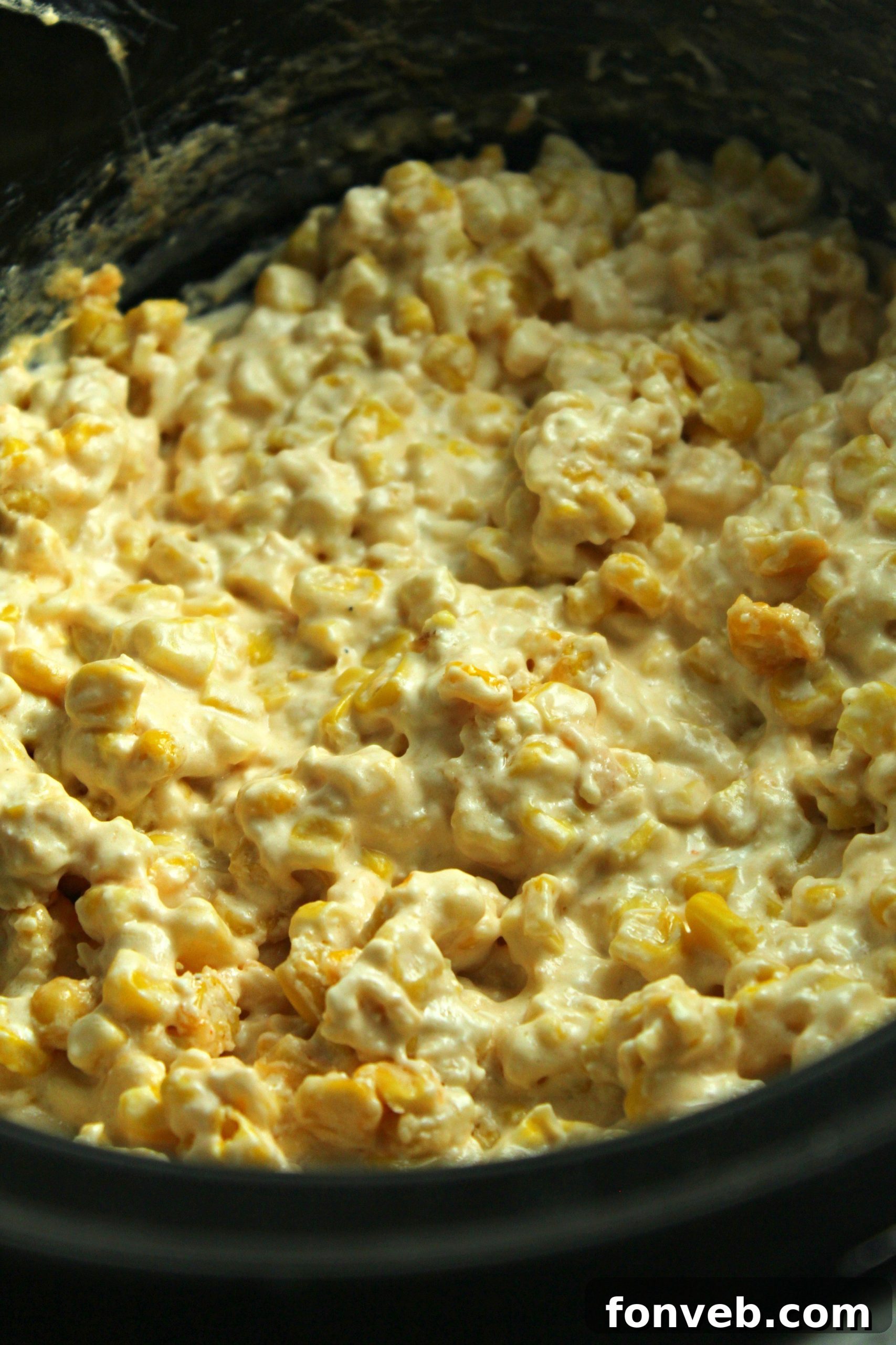 Close-up of creamy slow cooker cheesy corn with melted cheese pull, highlighting its indulgent texture.