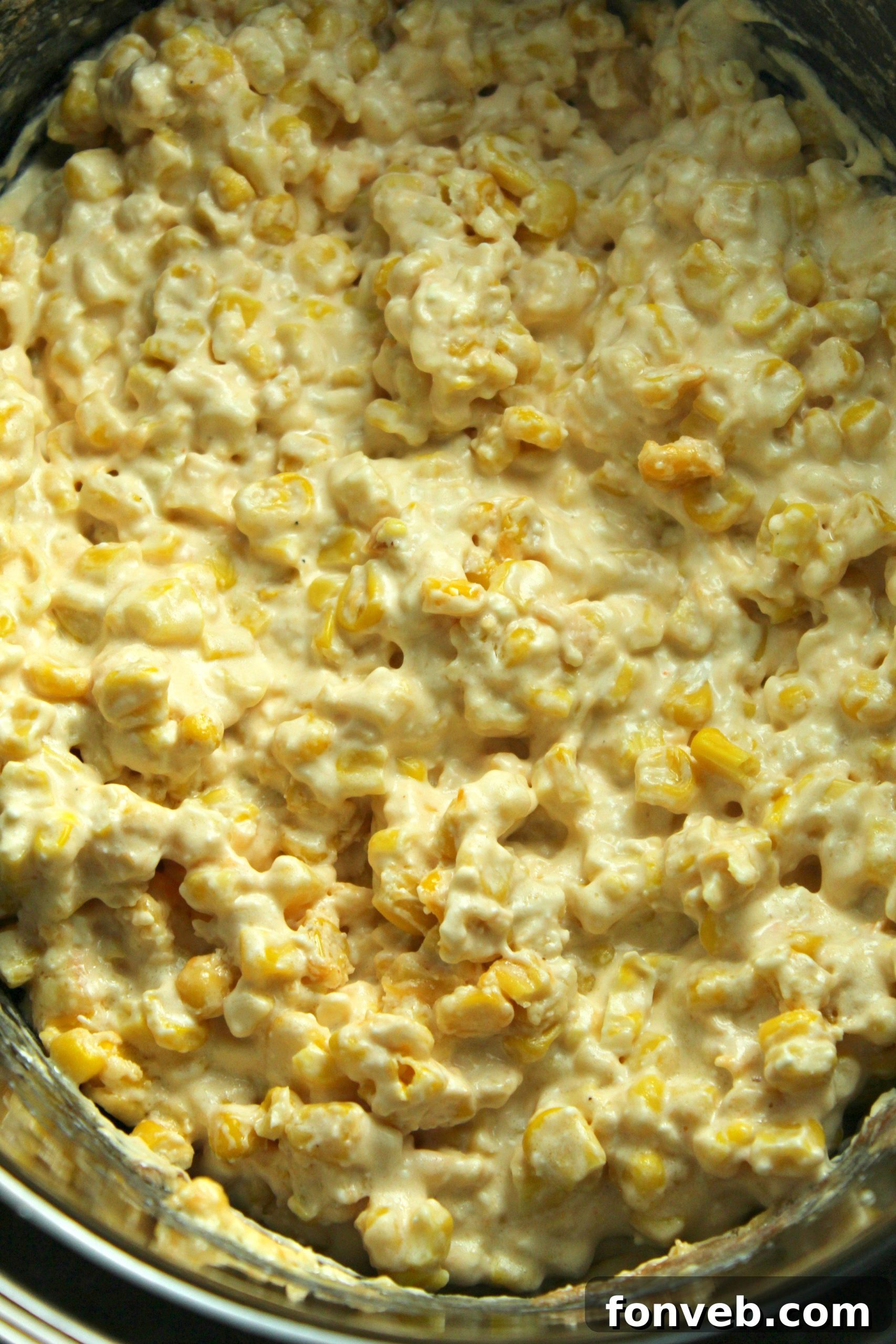 Full bowl of creamy slow cooker cheesy corn on a rustic wooden table, ready to be served.