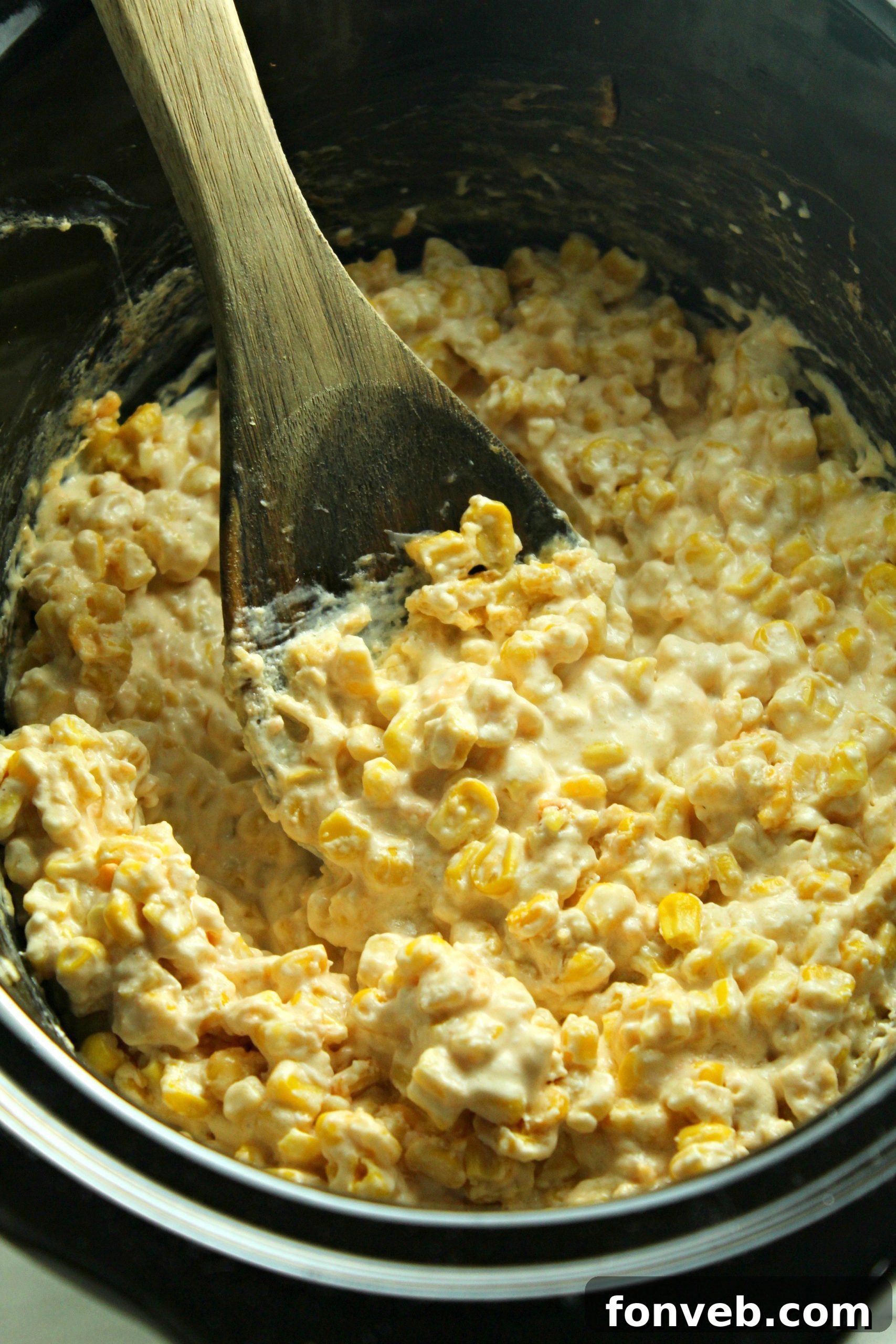 Close-up of creamy cheesy corn being stirred, showing the melted cheese and a few kernels.