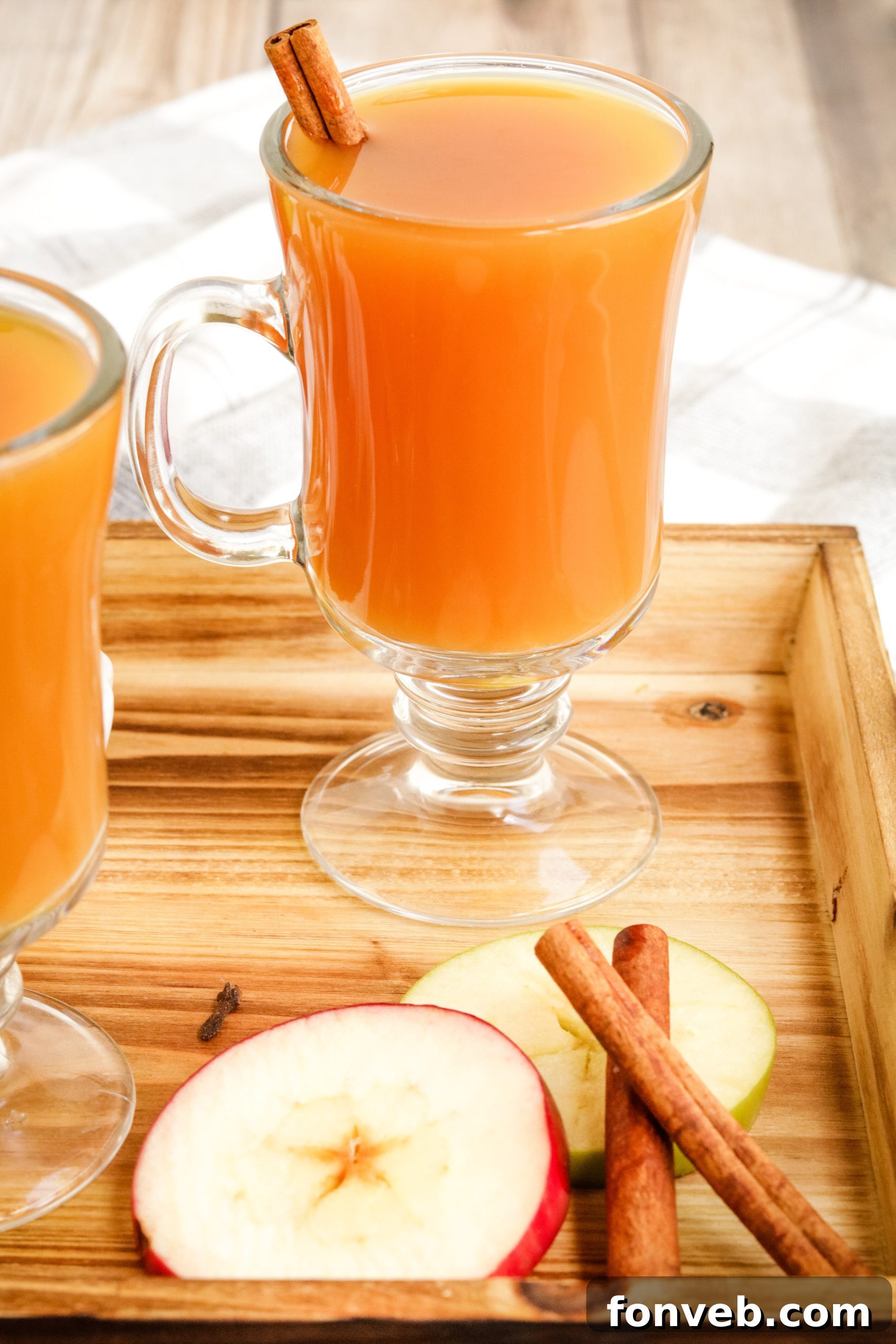 Cozy Slow Cooker Spiced Cider 8 Several mugs of hot mulled cider on a wooden tray, garnished with oranges and cinnamon, against a cozy backdrop.