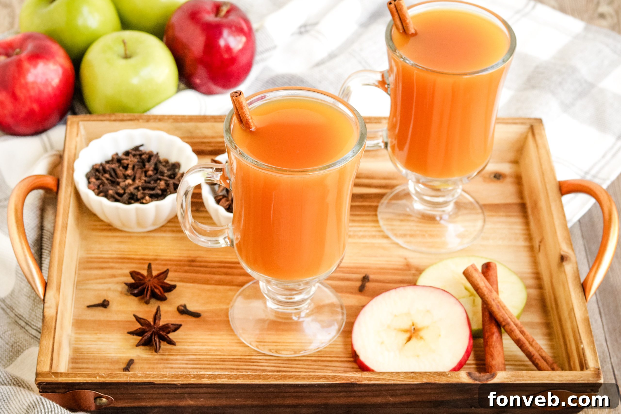 Cozy Slow Cooker Spiced Cider 9 Two clear mugs of mulled cider, garnished with orange slices and a cinnamon stick, on a dark wooden surface.