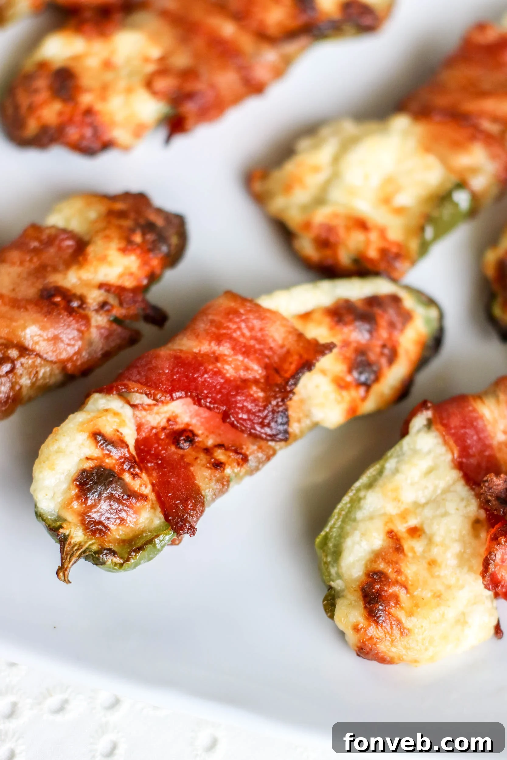 Crispy Keto Air Fryer Bacon Jalapeño Poppers 2 Close-up of freshly made Air Fryer Bacon Wrapped Jalapeno Poppers on a white plate, showcasing crispy bacon and melted cheese.