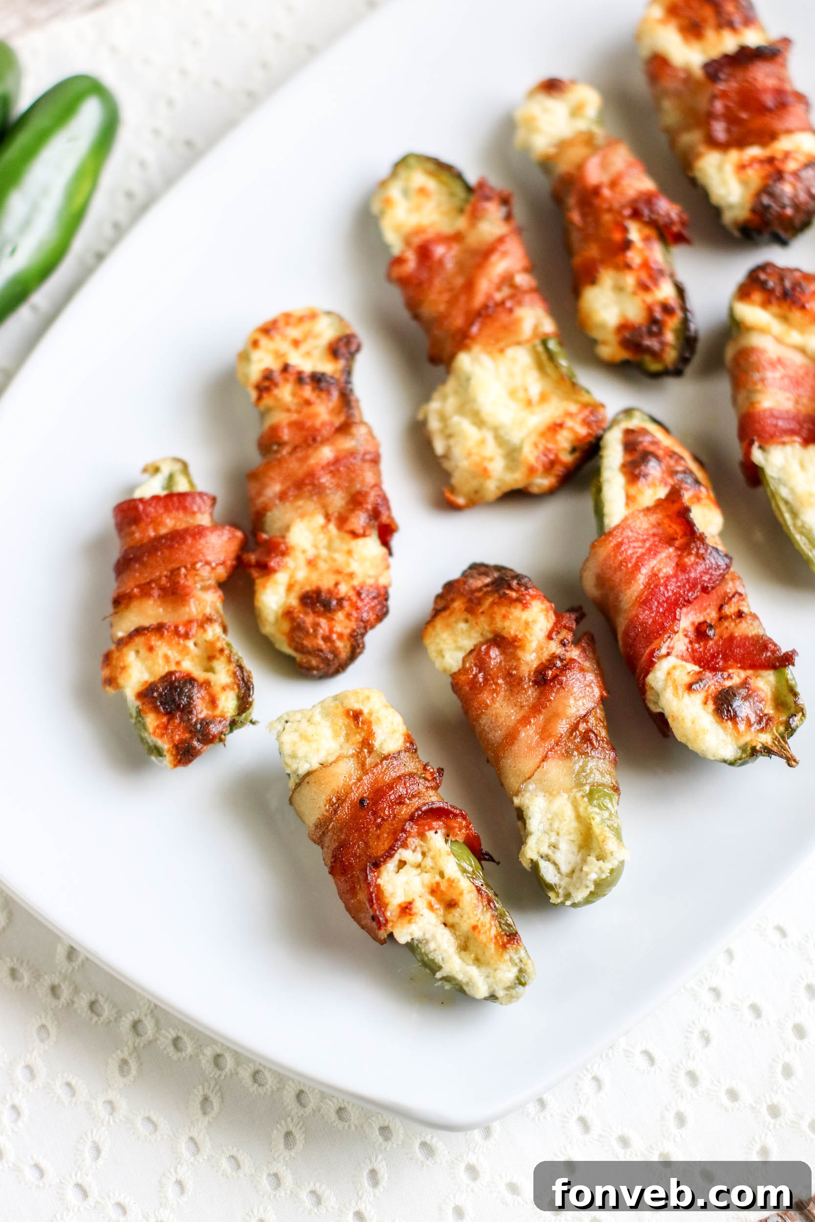 Crispy Keto Air Fryer Bacon Jalapeño Poppers 6 A top-down view of multiple Air Fryer Bacon Wrapped Jalapeno Poppers arranged on a rustic wooden board, garnished with fresh herbs.