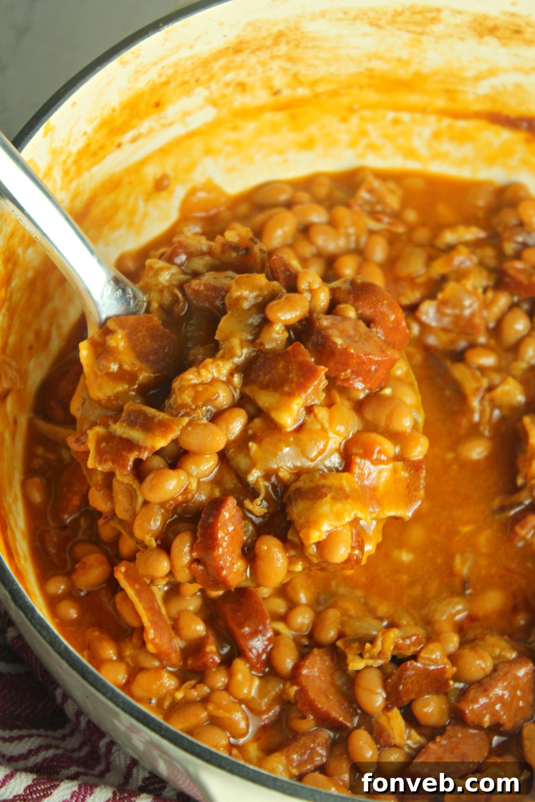 Signature Smoked Sausage Baked Beans 8 A large serving of Ultimate Baked Beans with Smoked Sausage in a rustic bowl