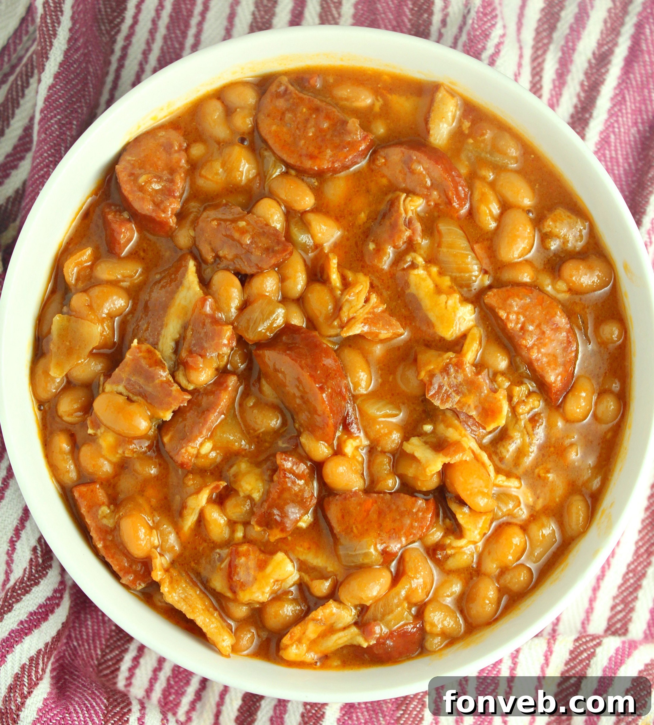Signature Smoked Sausage Baked Beans 10 Ultimate Baked Beans with Smoked Sausage in a Dutch oven, with a serving spoon and a small bowl on the side