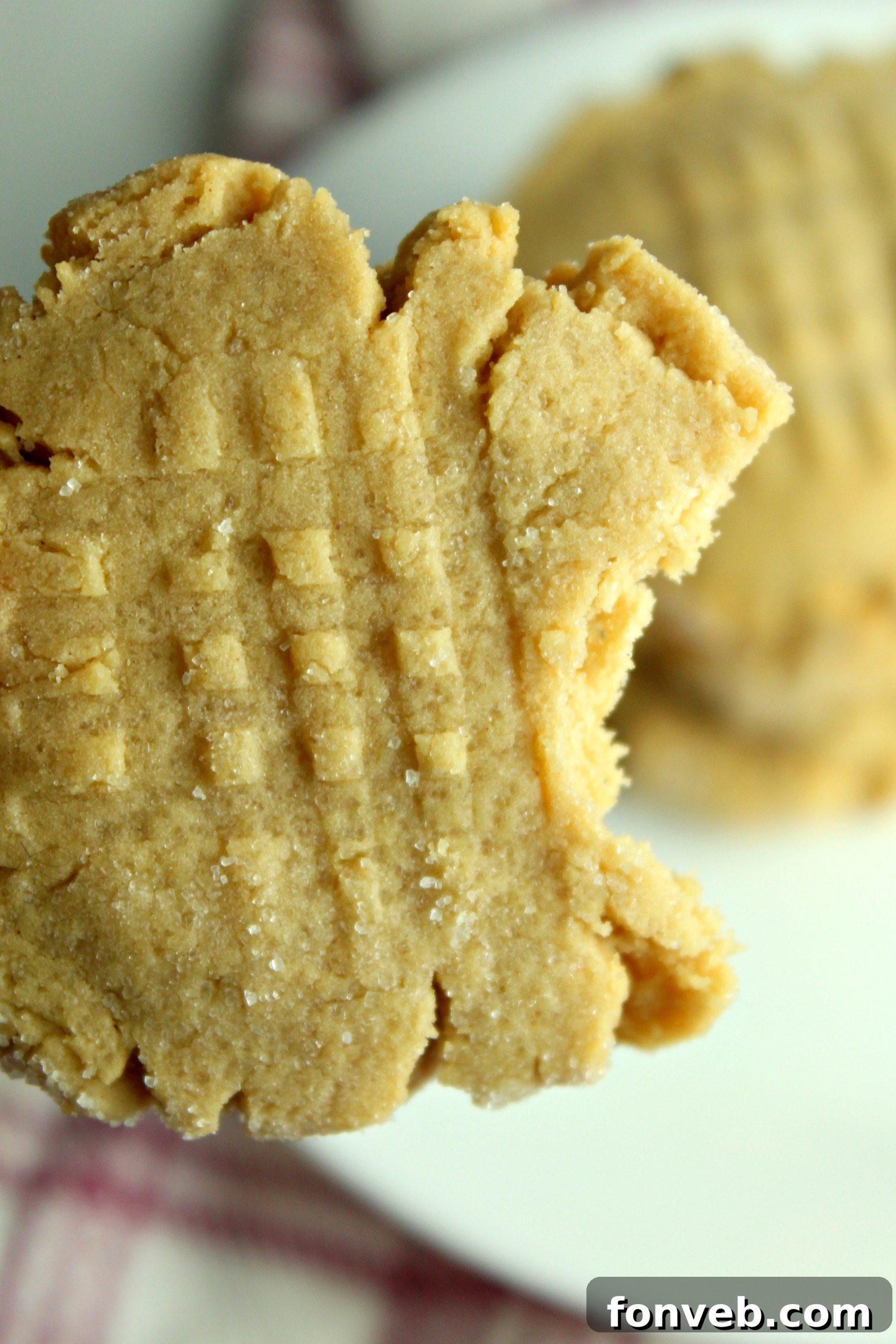 A close-up of a hand pressing a fork into a peanut butter cookie dough ball to create the criss-cross pattern before baking.