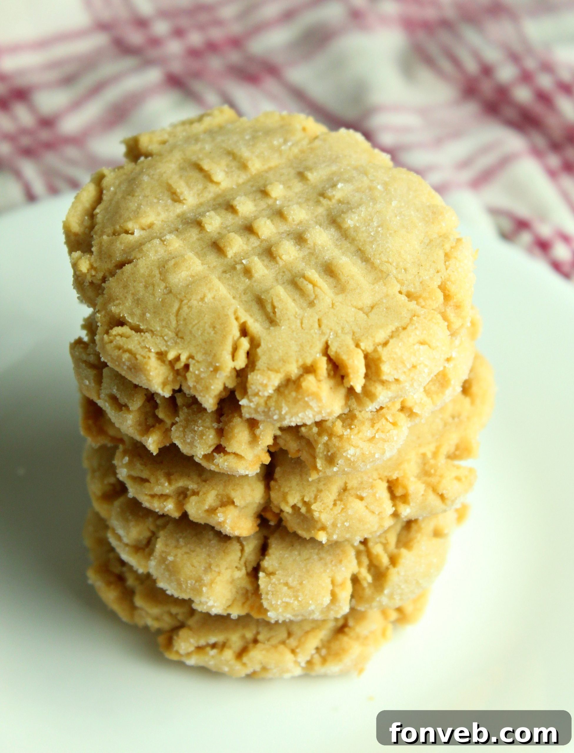 A close-up of several baked peanut butter cookies with a golden-brown hue and classic fork marks.