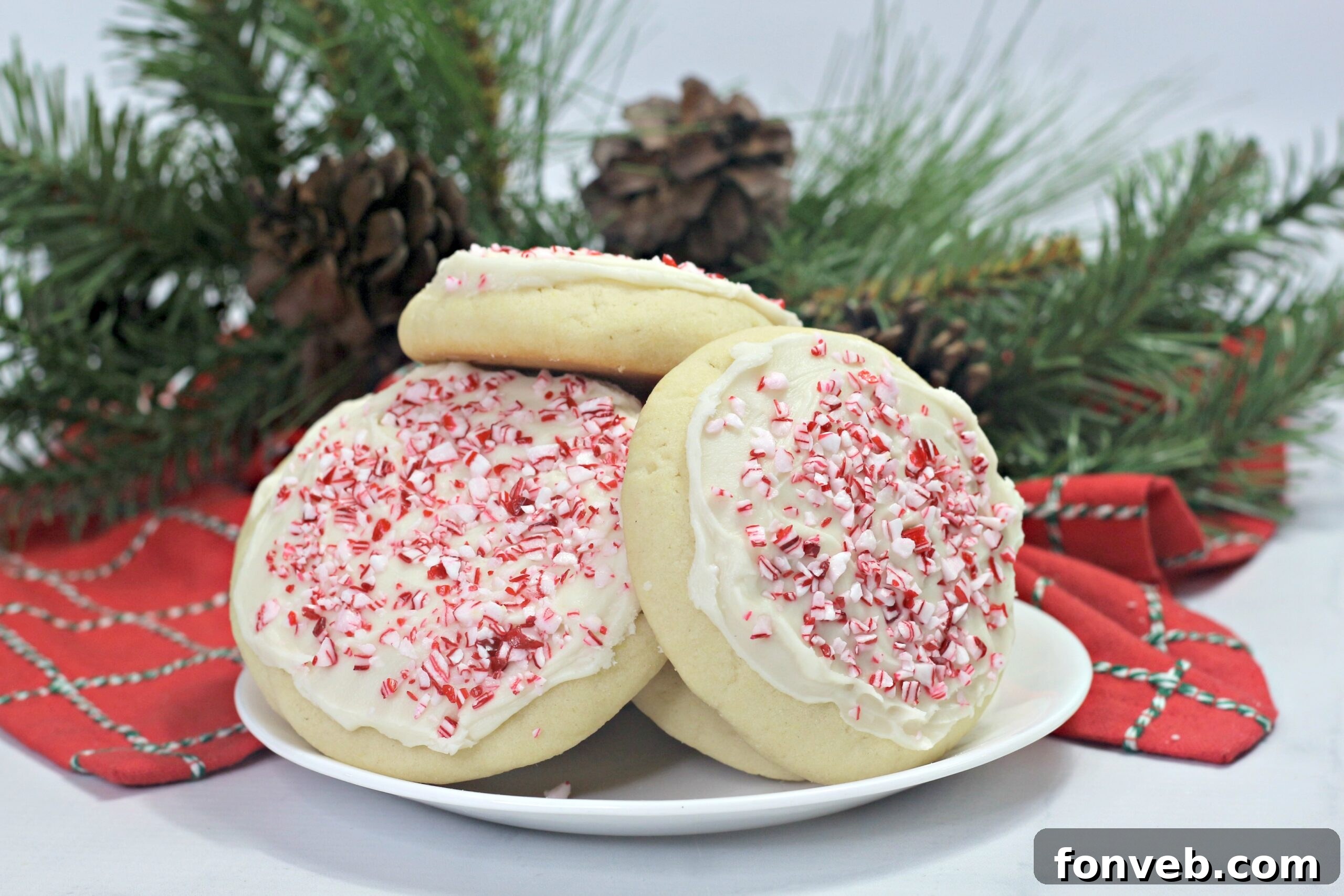 Close-up of three soft, thick Amish Sugar Cookies, some frosted with white icing and crushed candy canes, others with vibrant sprinkles, arranged on a rustic wooden surface.