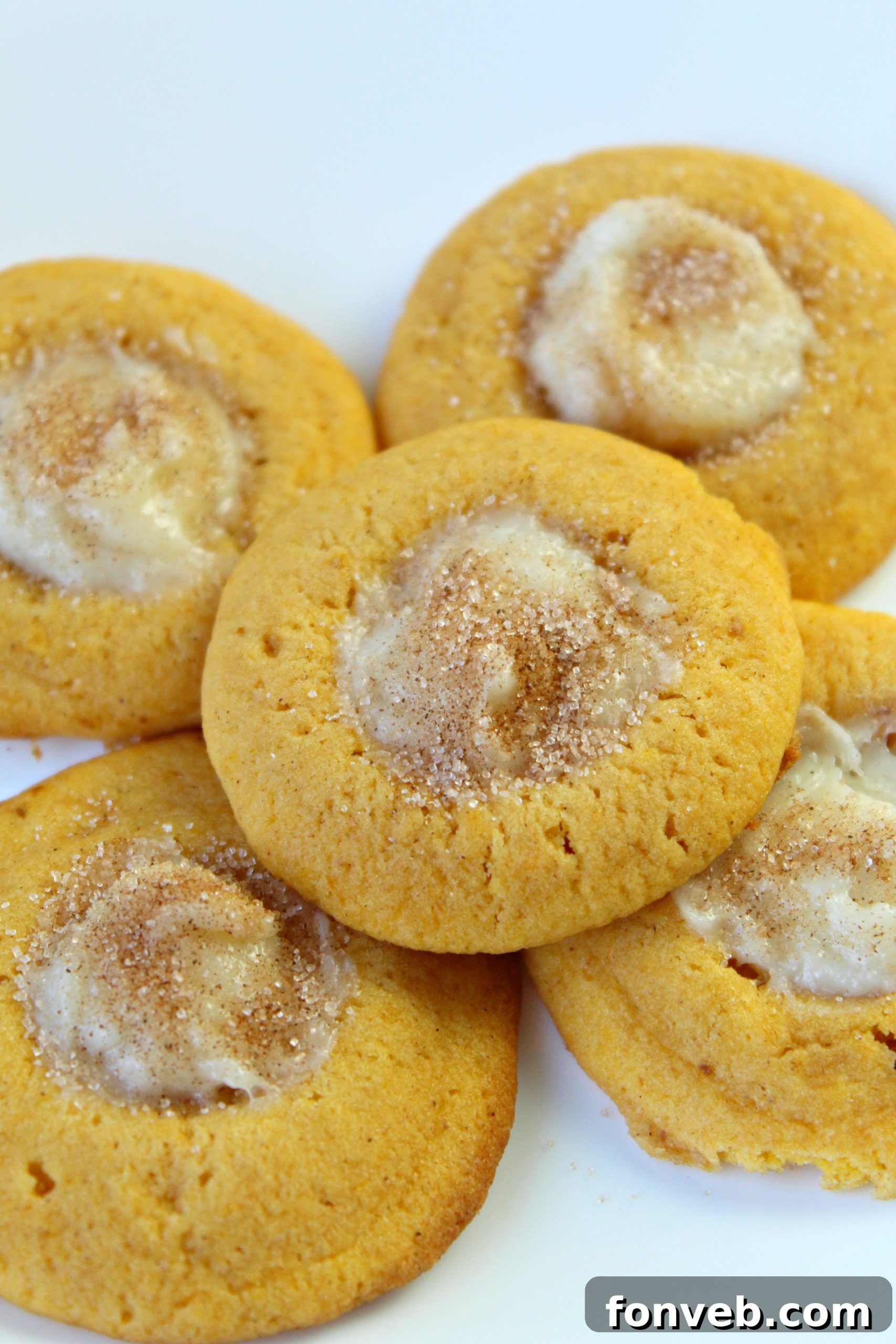 Freshly baked pumpkin thumbprint cookies with a creamy cheesecake center, dusted with cinnamon sugar, on a cooling rack.