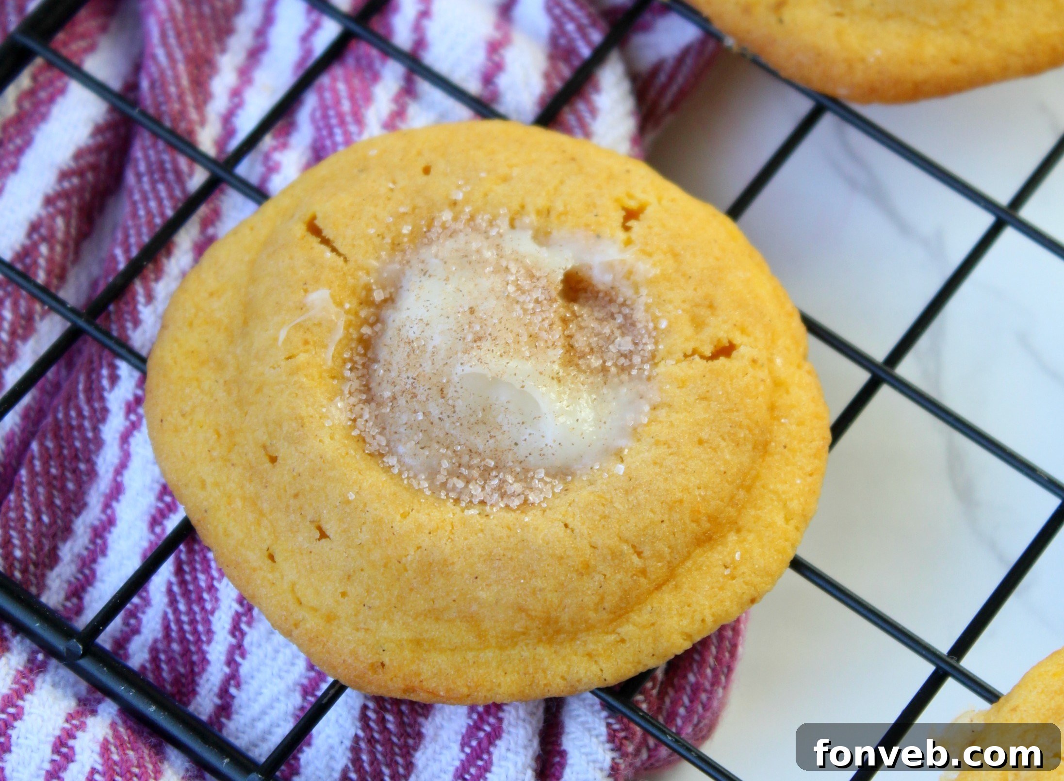 A close-up of classic Raspberry Almond Thumbprint Cookies, featuring a golden cookie base and a vibrant red jam center.