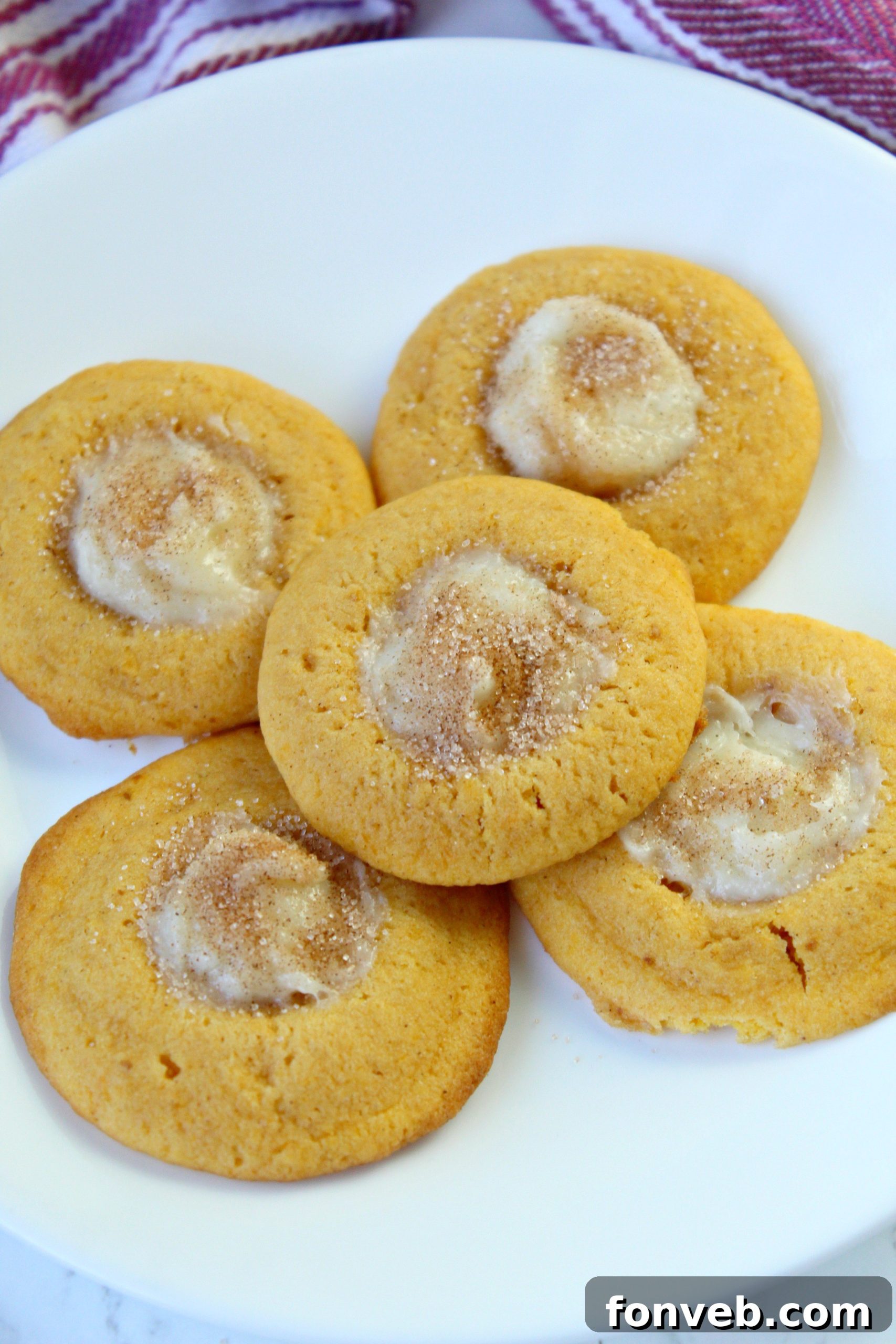 A close-up of Pumpkin Cheesecake Thumbprint Cookies on a wire rack, showcasing the rich pumpkin color and delicate sugar dusting.